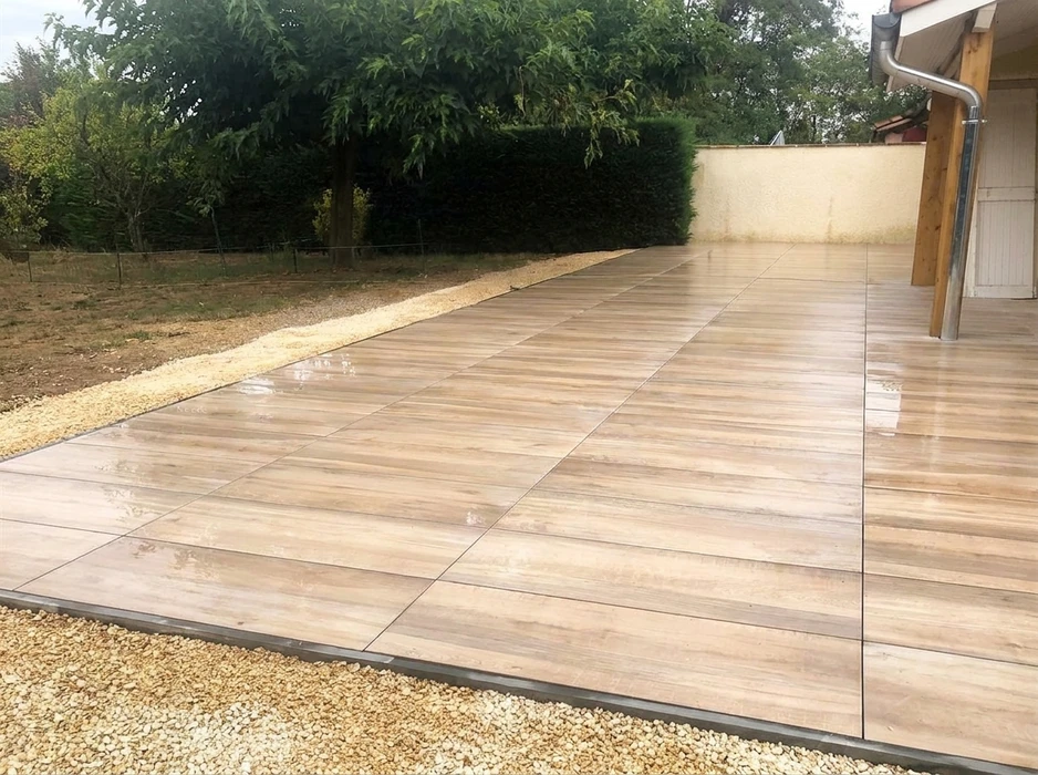 Terrasse extérieure récemment posée, mouillée par la pluie, bordée de gravier décoratif