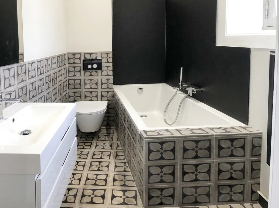 Salle de bains moderne avec baignoire encastrée rectangulaire, WC suspendu avec plaque de commande double touche noire, vasque à poser sur meuble blanc laqué