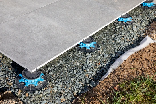 Ouvrier en extérieur installant un carrelage de grandes dalles grises sur une terrasse